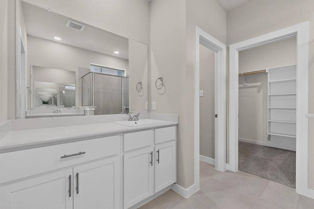 6001 Kaitlynn Drive, Princeton, TX 75071 White vanity featuring shaker-style cabinetry, matte black hardware, and a solid-surface countertop with an integrated basin, complemented by a large wall-mounted mirror and built-in closet shelving