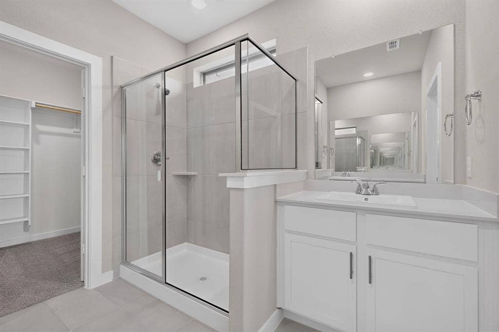 6001 Kaitlynn Drive, Princeton, TX 75071 Frameless glass-enclosed shower with tiled surround, white vanity cabinetry with integrated sink, polished hardware, large wall-mounted mirror, and built-in closet shelving