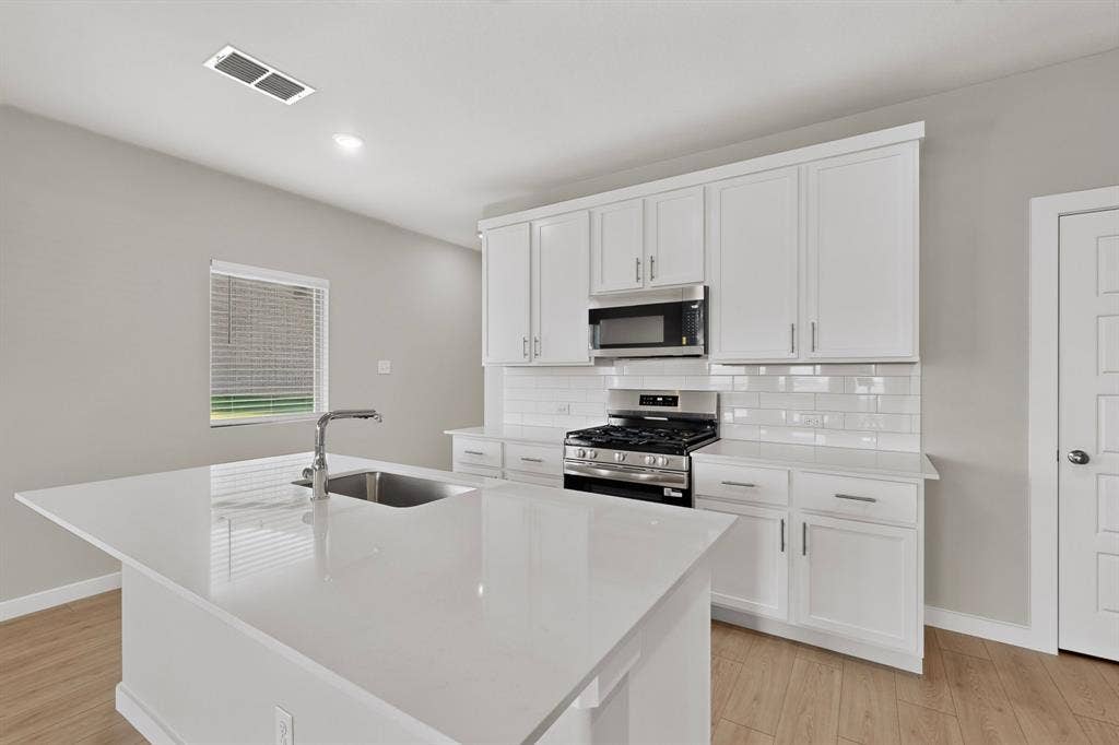 6001 Kaitlynn Drive, Princeton, TX 75071 Kitchen featuring white cabinetry, solid-surface countertops, a center island with an integrated stainless steel sink, subway tile backsplash, and wood-finish flooring