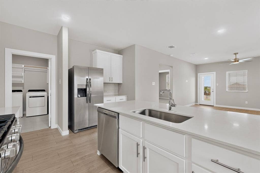 6001 Kaitlynn Drive, Princeton, TX 75071 Kitchen featuring an expansive center island with solid-surface countertop, undermount stainless steel sink, white shaker-style cabinetry, and wood-finish flooring