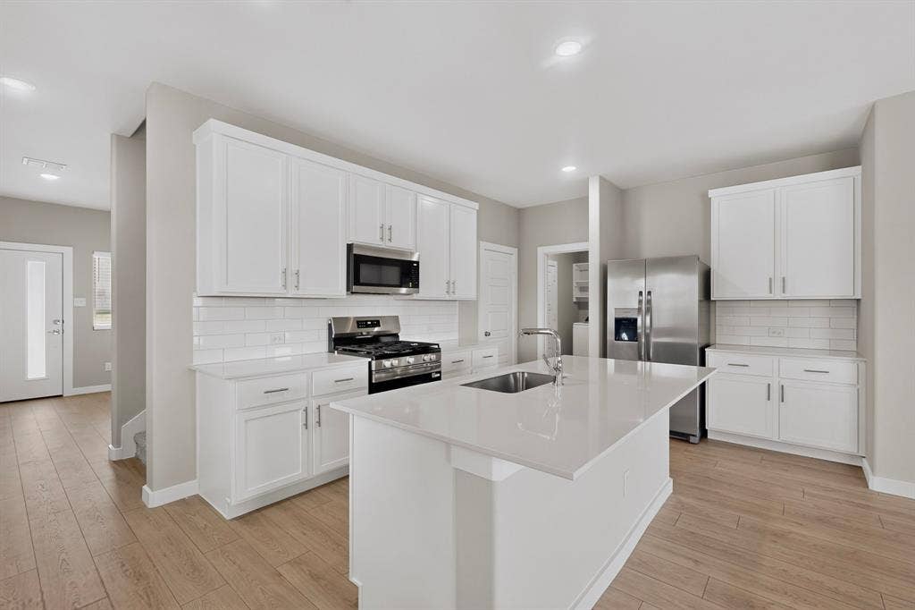 6001 Kaitlynn Drive, Princeton, TX 75071 Kitchen featuring white cabinetry, quartz countertops, a central island with a stainless steel undermount sink, subway tile backsplash, and wood-finish flooring