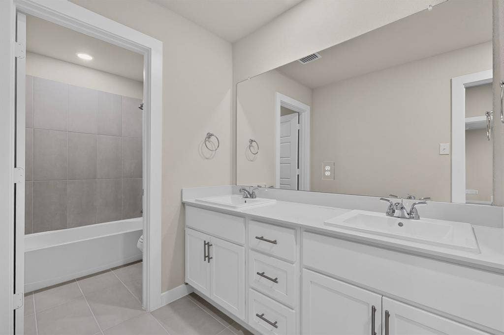 6001 Kaitlynn Drive, Princeton, TX 75071 Dual-sink vanity with white cabinetry, solid-surface countertop, polished chrome fixtures, and a full-width vanity mirror