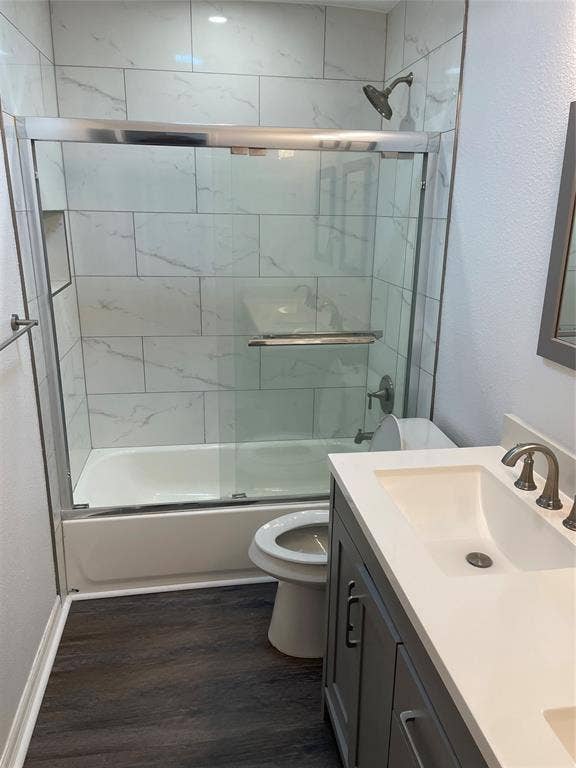 1423 Northridge Drive, Carrollton, TX 75006 Bathroom featuring wood-finish flooring, a vanity with a solid-surface countertop and undermount sink, shower-tub combination with sliding glass doors, and full-height tiled surround with a built-in recessed niche