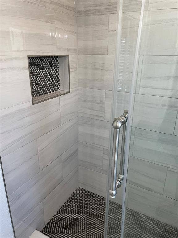 1423 Northridge Drive, Carrollton, TX 75006 Walk-in shower featuring large-format horizontal tile walls, a built-in recessed tiled niche, black penny tile flooring, and a glass enclosure with a metallic pull handle