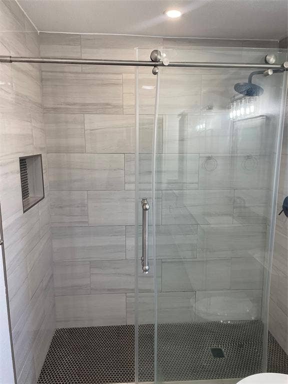 1423 Northridge Drive, Carrollton, TX 75006 Walk-in shower featuring large-format neutral wall tile, circular mosaic floor tile, brushed nickel sliding glass door hardware, a recessed wall niche, and a rain-style shower head