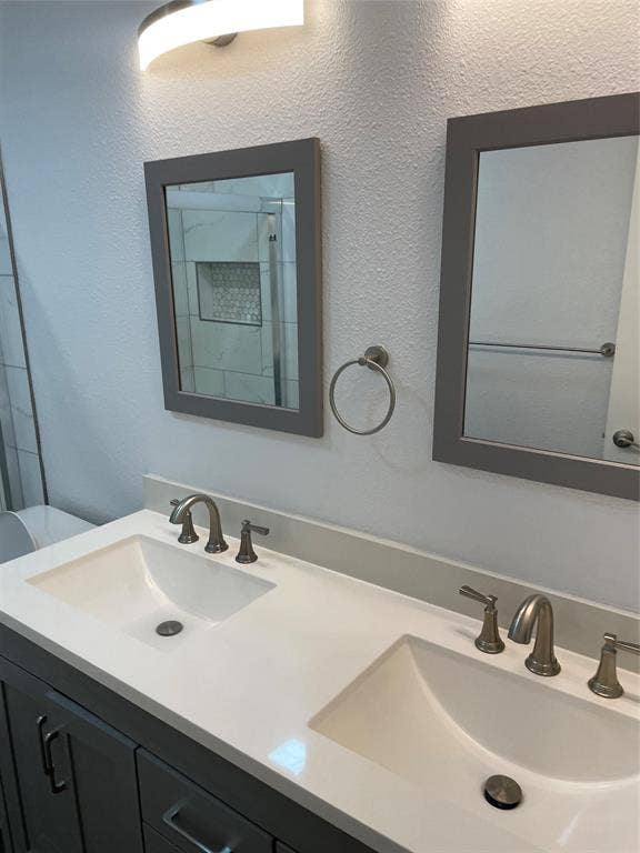 1423 Northridge Drive, Carrollton, TX 75006 Double vanity featuring a light-toned countertop with integrated dual sinks, brushed nickel widespread faucets, framed mirrors, and a wall-mounted light fixture