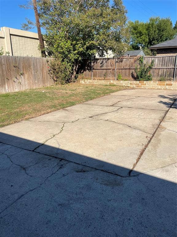 1423 Northridge Drive, Carrollton, TX 75006 Outdoor area featuring a concrete slab, a natural grass lawn, a wood perimeter fence, and a stone retaining wall