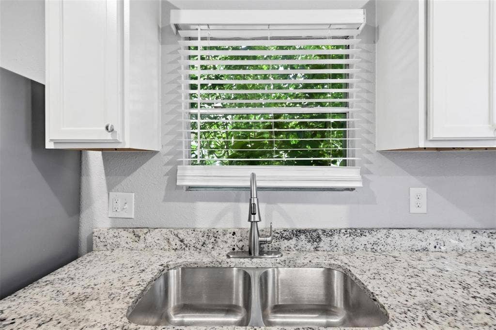 1227 Wilbur Street, Dallas, TX 75224 Double basin stainless steel sink with a high-arch pull-down faucet, light-toned stone-finish countertop, white cabinetry, and horizontal window blinds