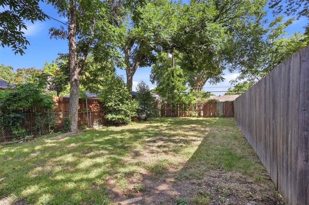 1227 Wilbur Street, Dallas, TX 75224 Rear yard featuring grass landscaping, mature trees, and wooden perimeter fencing