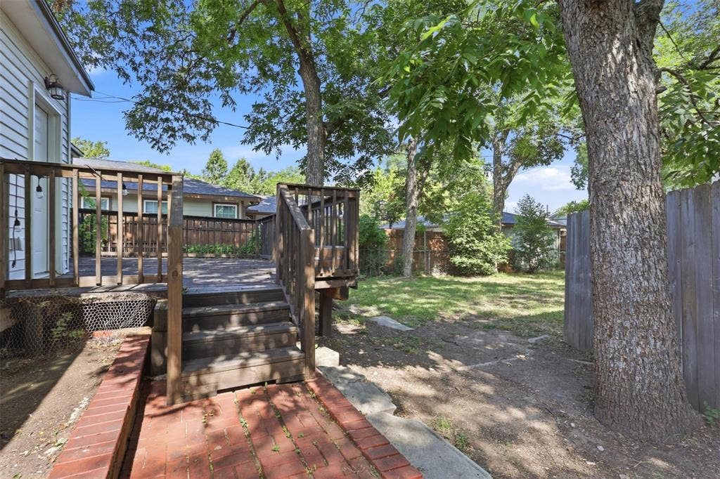1227 Wilbur Street, Dallas, TX 75224 Raised wood deck with integrated stairs, red brick pathway, and mature trees providing partial shade within a fenced outdoor area