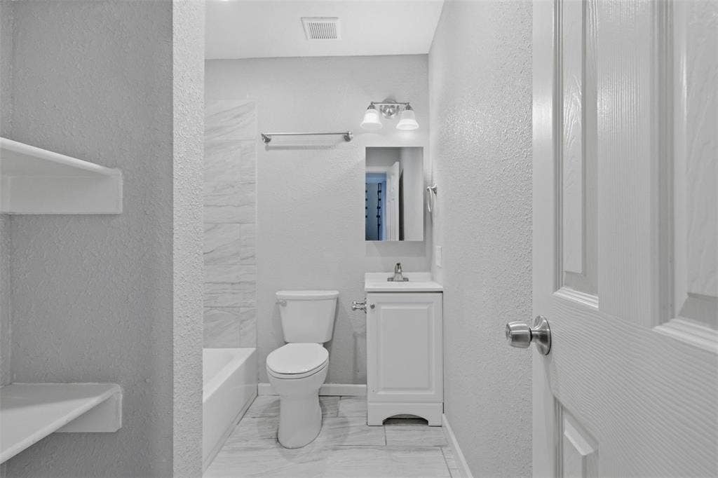 1227 Wilbur Street, Dallas, TX 75224 Full bathroom featuring a white vanity cabinet with a stone-top sink, tub-shower combination with light-toned wall tile, built-in recessed shelving, and a dual-light fixture