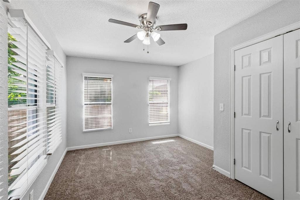 1227 Wilbur Street, Dallas, TX 75224 Neutral-toned room featuring carpeted flooring, two double-panel windows with adjustable horizontal blinds, a ceiling fan with integrated light fixture, and a white paneled closet door