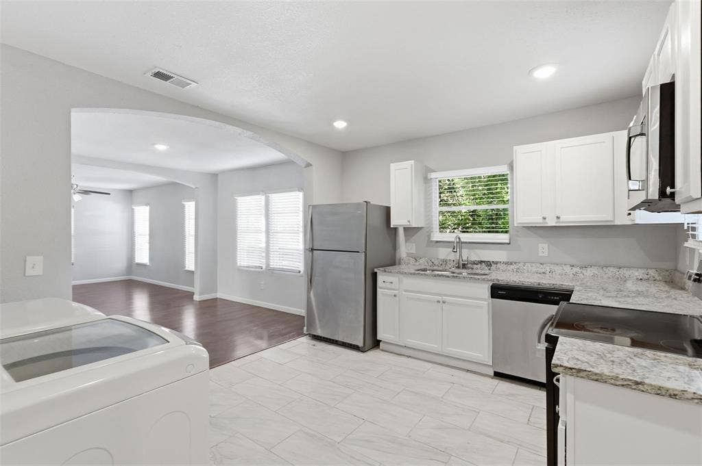 1227 Wilbur Street, Dallas, TX 75224 Kitchen featuring white cabinetry, stone-finish countertops, stainless steel appliances, and large-format tile flooring, highlighted by an arched architectural opening