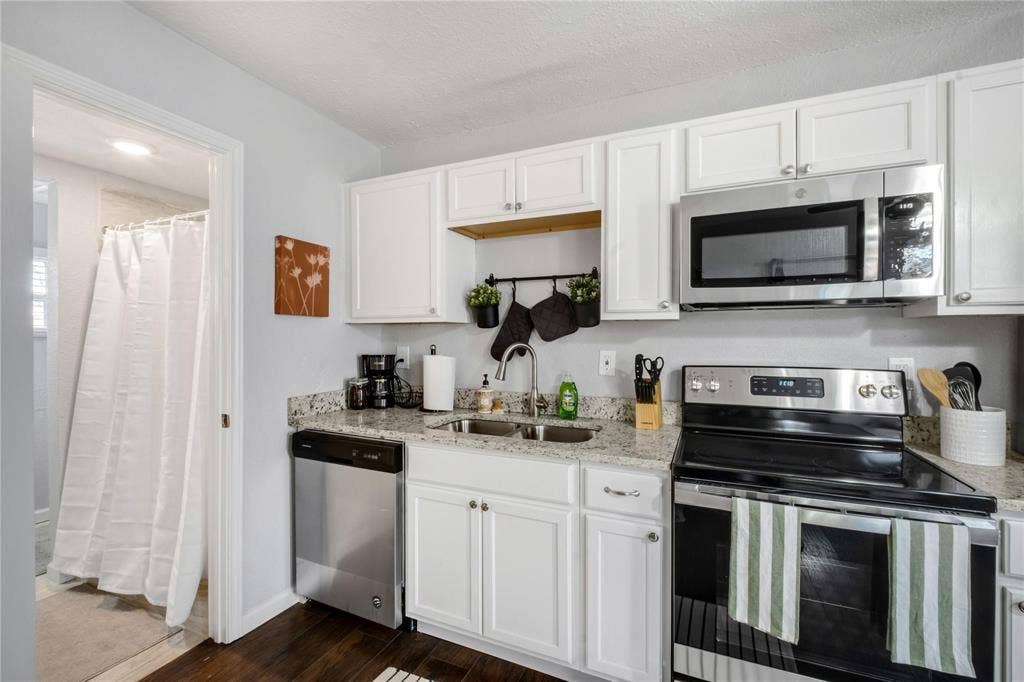 1227 Wilbur Street, Dallas, TX 75224 Kitchen featuring white shaker-style cabinetry, stone-finish countertops, stainless steel appliances, and wood-finish flooring
