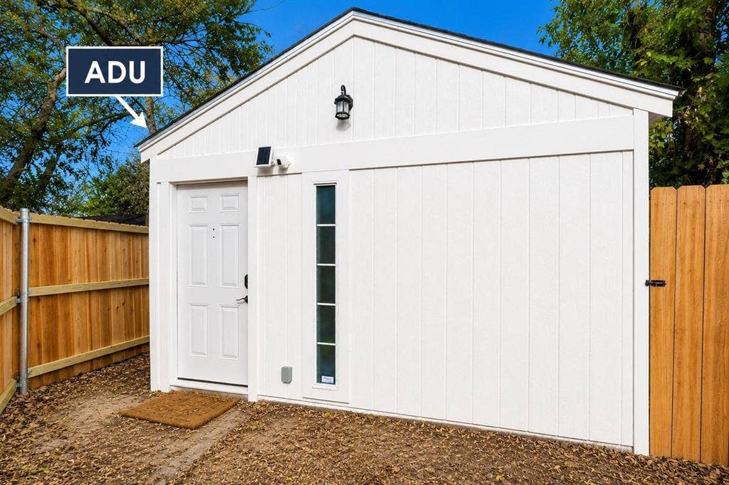 1227 Wilbur Street, Dallas, TX 75224 Detached accessory dwelling unit featuring white board-and-batten siding, a gable roofline, vertical fixed window, and exterior wall-mounted lighting