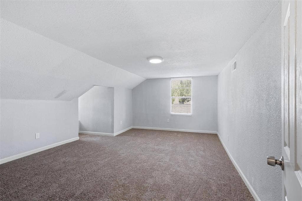 1227 Wilbur Street, Dallas, TX 75224 Interior room featuring neutral wall-to-wall carpeting, angled ceiling architecture, a single-pane window, and a flush-mount ceiling light fixture