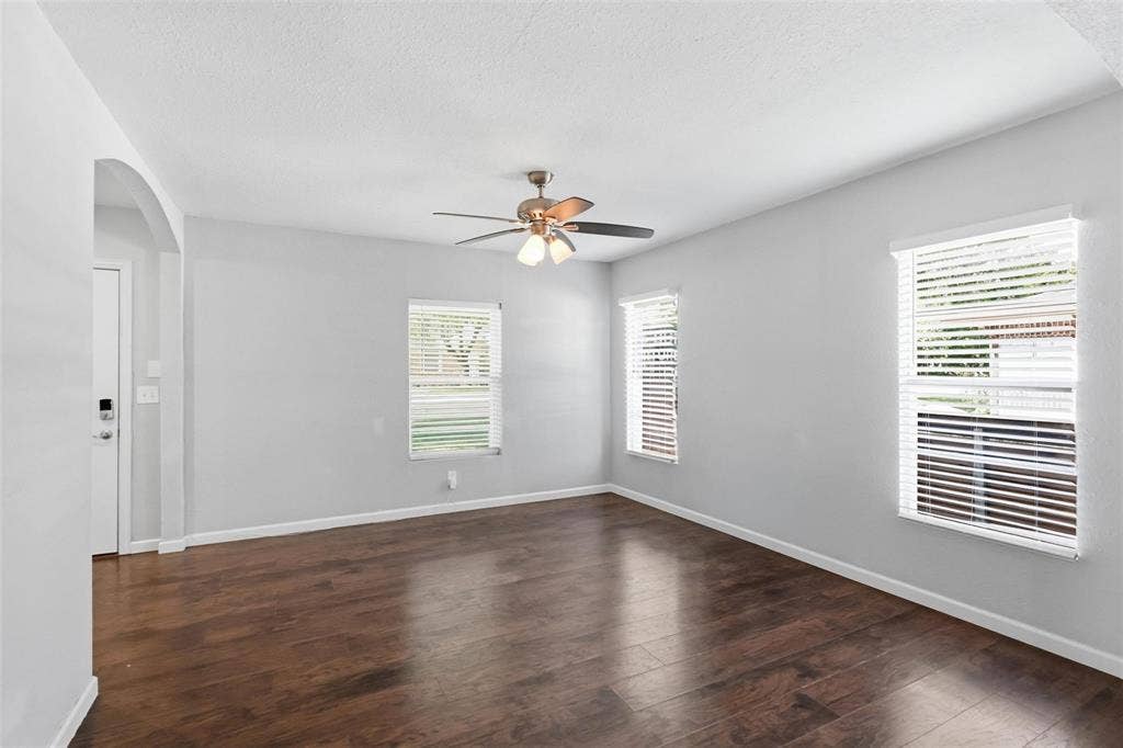 1227 Wilbur Street, Dallas, TX 75224 Neutral interior space featuring wood-finish flooring, white walls, multiple windows with horizontal blinds, and a central ceiling fan with integrated lighting