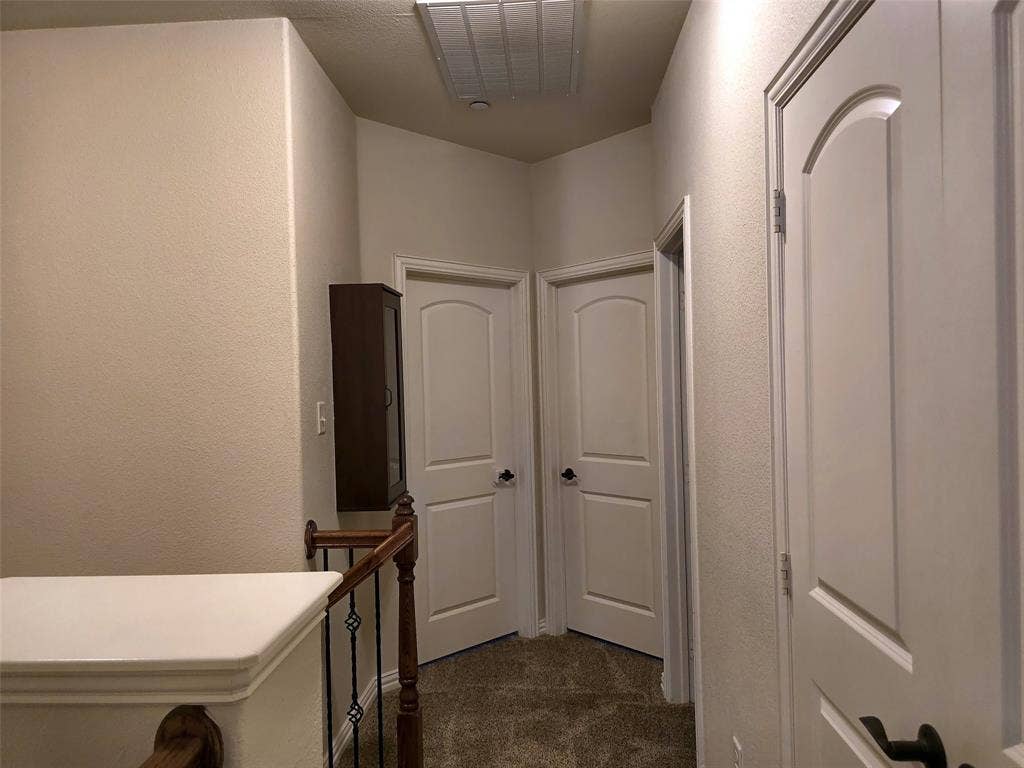 1504 Fox Run Drive, Irving, TX 75063 Hallway featuring three arched-panel interior doors, neutral wall-to-wall carpeting, and a wooden handrail with vertical metal spindles