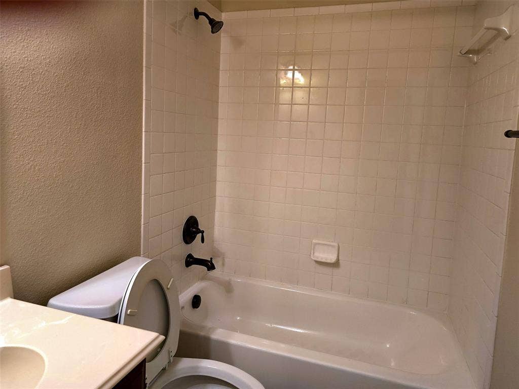 1504 Fox Run Drive, Irving, TX 75063 Full-size bathtub with white tile surround, matte black showerhead and faucet, built-in soap dish, and vanity with integrated countertop