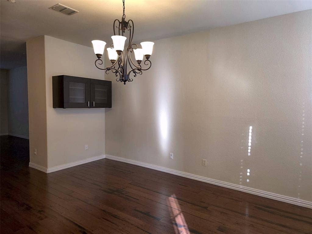 1504 Fox Run Drive, Irving, TX 75063 Wood-finish flooring, dark-toned wall-mounted cabinetry with glass-panel doors, and an ornate metal chandelier featuring five frosted-glass shades
