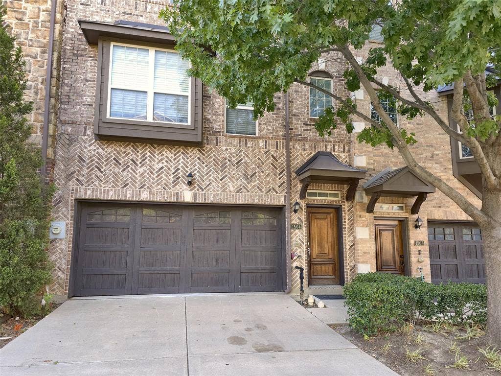 1504 Fox Run Drive, Irving, TX 75063 Multi-story brick exterior featuring herringbone masonry detailing, a two-car garage with overhead carriage-style doors, wooden entry doors, and metal-covered entry overhangs