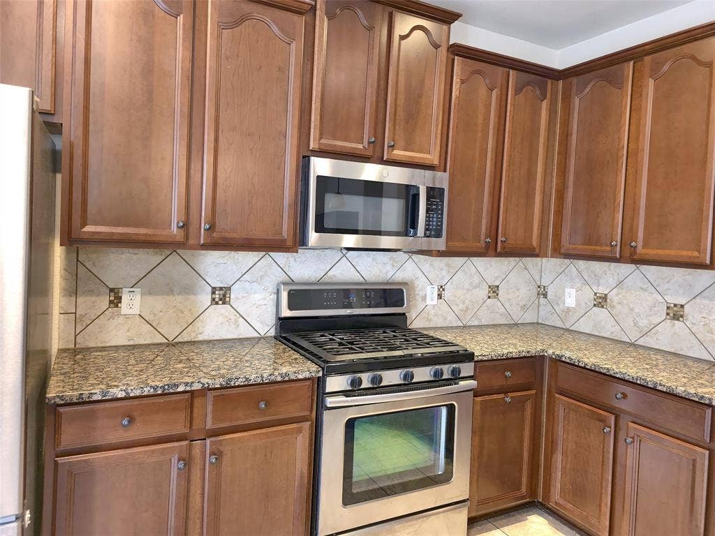1504 Fox Run Drive, Irving, TX 75063 Kitchen featuring stained wood cabinetry, stone countertops, stainless steel gas range, over-the-range microwave, and a tile backsplash with decorative accents