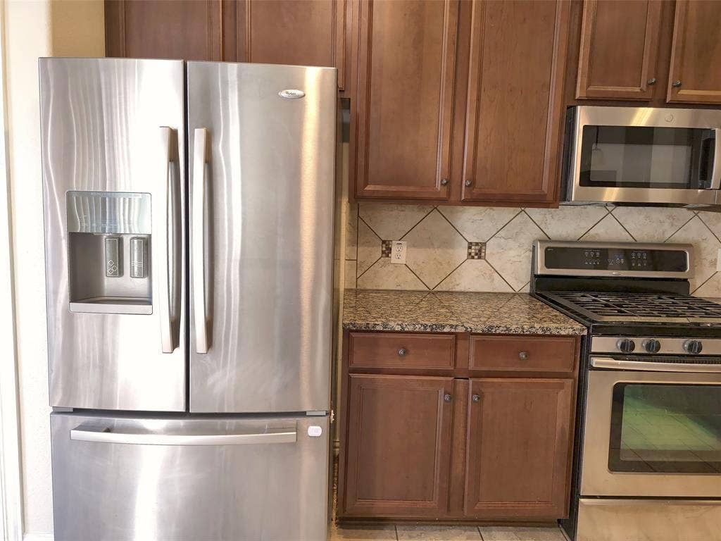 1504 Fox Run Drive, Irving, TX 75063 Stainless steel French door refrigerator, built-in microwave, gas range, wood cabinetry, and stone-tiled backsplash