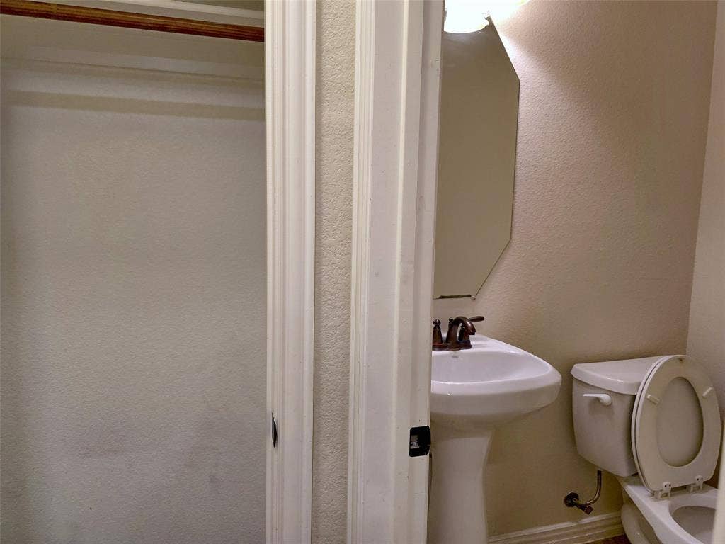 1504 Fox Run Drive, Irving, TX 75063 Pedestal sink with a dual-handle metal faucet, wall-mounted geometric mirror, and built-in closet storage