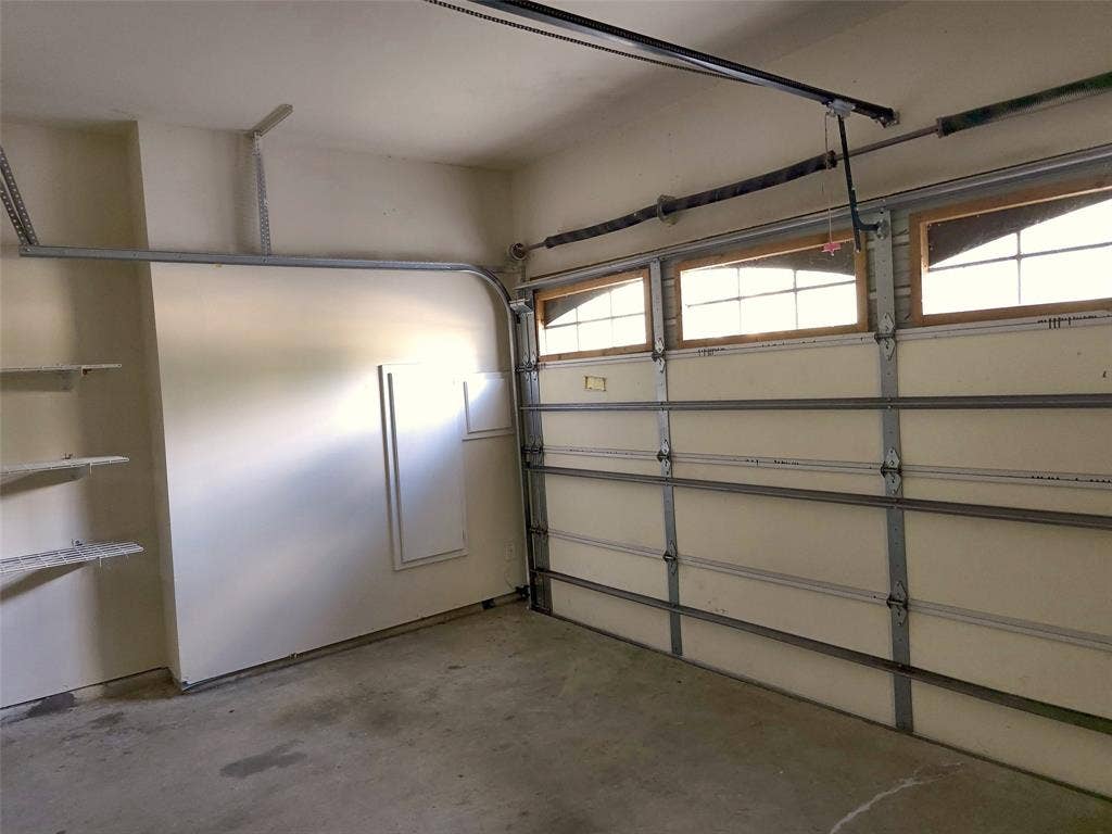 1504 Fox Run Drive, Irving, TX 75063 Garage interior featuring a sectional paneled door with integrated transom windows, exposed ceiling-mounted door hardware, and built-in wall shelving