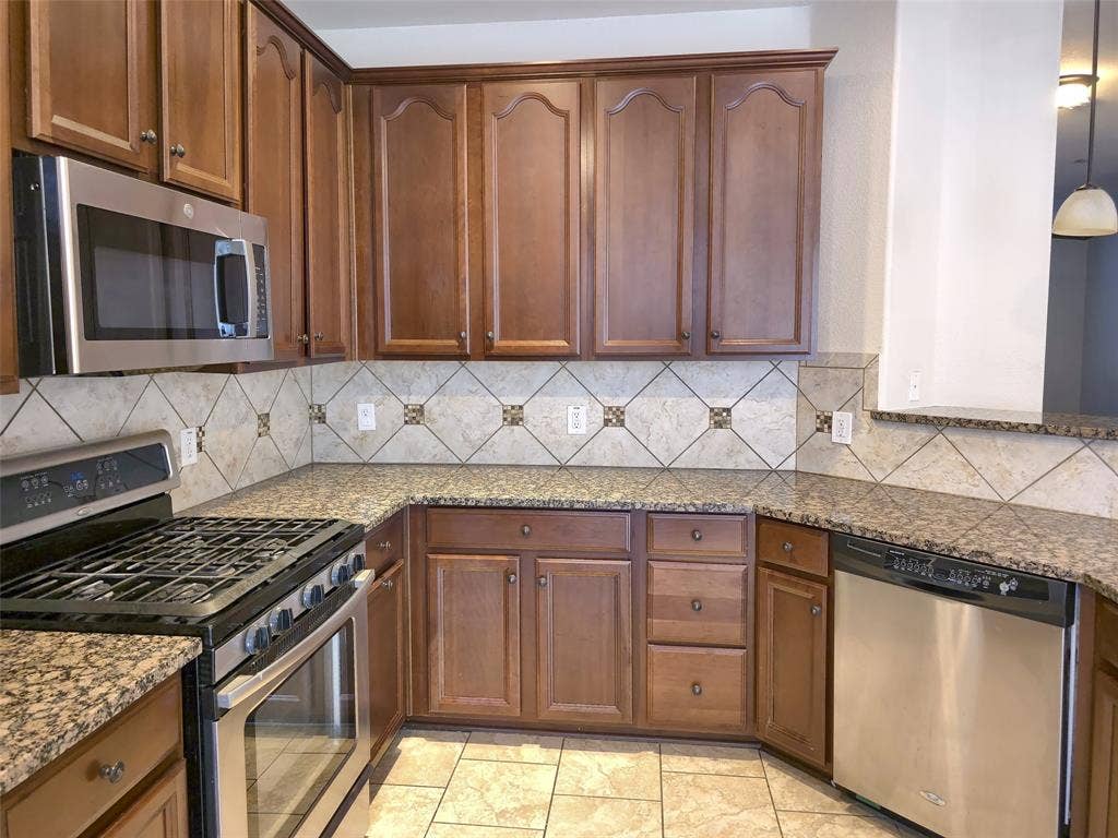 1504 Fox Run Drive, Irving, TX 75063 Kitchen featuring stained wood cabinetry, stone-finish countertops, stainless steel appliances, a diamond-pattern tile backsplash with decorative accents, and tiled flooring