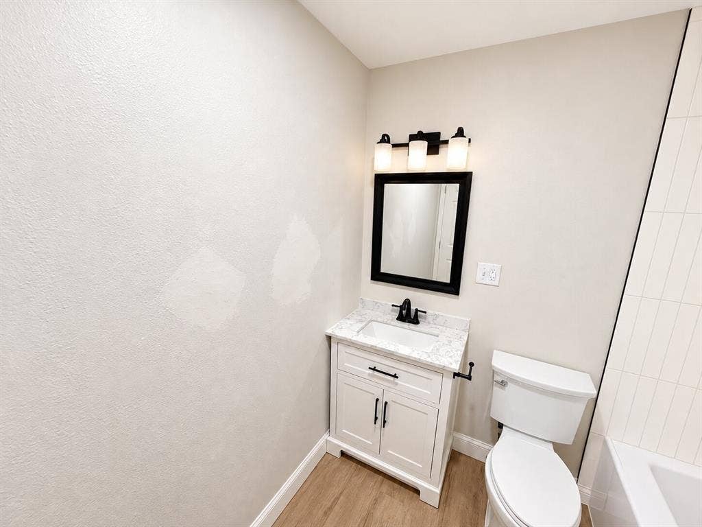 1307 Crestridge Drive, Plano, TX 75075 Vanity featuring a stone-look countertop, integrated rectangular sink, matte black faucet, shaker-style cabinetry, and three-light wall-mounted fixture