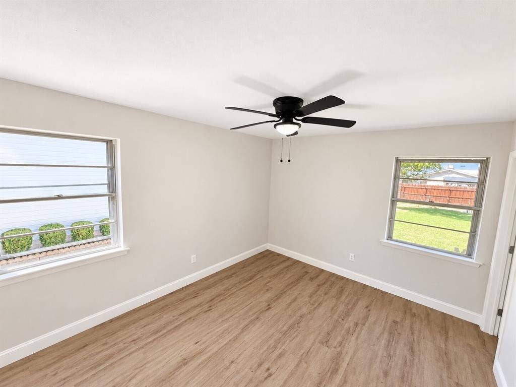 1307 Crestridge Drive, Plano, TX 75075 Neutral wall tones paired with wood-finish flooring, dual windows with exterior window bars, and a matte black ceiling fan with an integrated light fixture