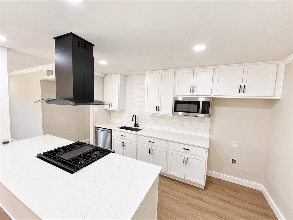 1307 Crestridge Drive, Plano, TX 75075 Kitchen featuring a central island with a built-in gas cooktop, quartz countertops, white cabinetry, matte black fixtures, and wood-finish flooring