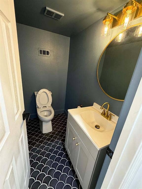 5864 Oram Street, Dallas, TX 75206 Powder room featuring patterned scalloped floor tile, vanity with integrated basin, brass-finish faucet and hardware, round gold-framed mirror, and multi-bulb wall lighting