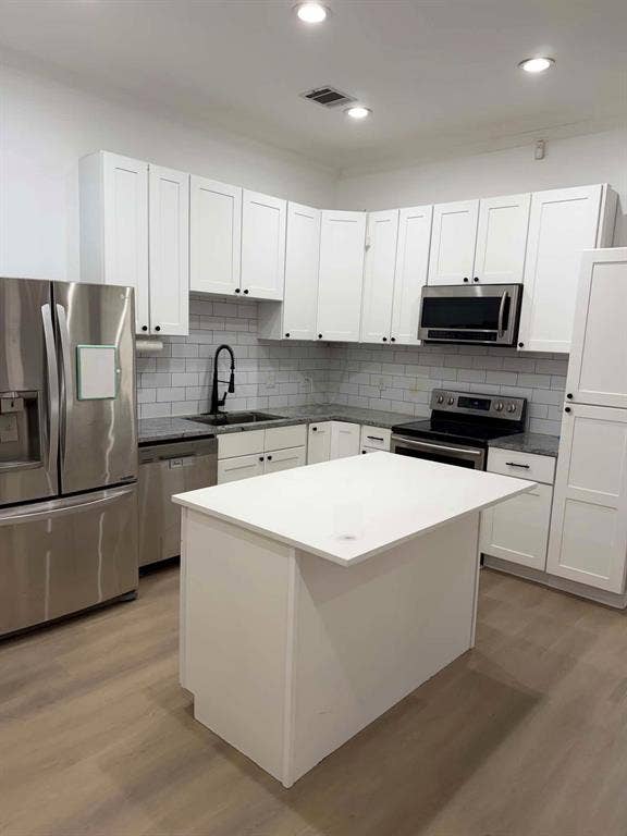 5864 Oram Street, Dallas, TX 75206 Kitchen featuring white shaker-style cabinetry, stone countertops, a subway tile backsplash, stainless steel appliances, and wood-finish flooring