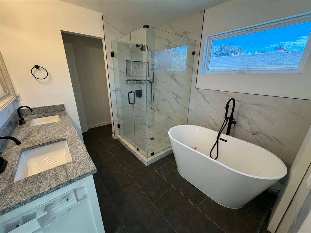 5864 Oram Street, Dallas, TX 75206 Bathroom featuring a dual-sink vanity with stone countertops, a standalone soaking tub with matte black fixtures, and a glass-enclosed walk-in shower with tile wall surround
