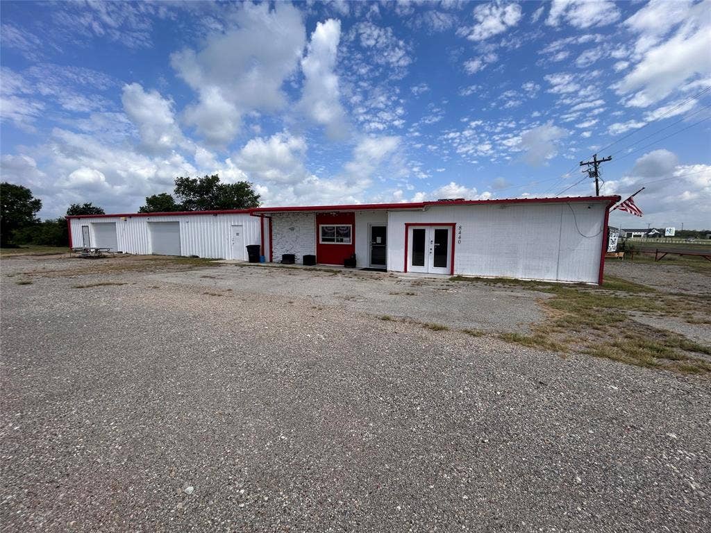 8440 E Highway 175 Highway, Kemp, TX 75143 Single-story commercial building featuring white vertical siding, red trim detailing, multiple exterior access points, and a gravel lot