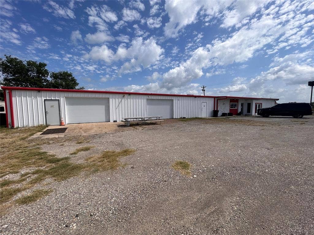 8440 E Highway 175 Highway, Kemp, TX 75143 Metal-sided exterior building featuring two overhead garage doors, multiple exterior entry points, and a spacious gravel lot
