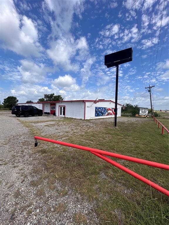 8440 E Highway 175 Highway, Kemp, TX 75143 Single-story commercial building featuring white metal siding, a red metal roof, a prominent freestanding electronic signage pylon, and a gated gravel entrance