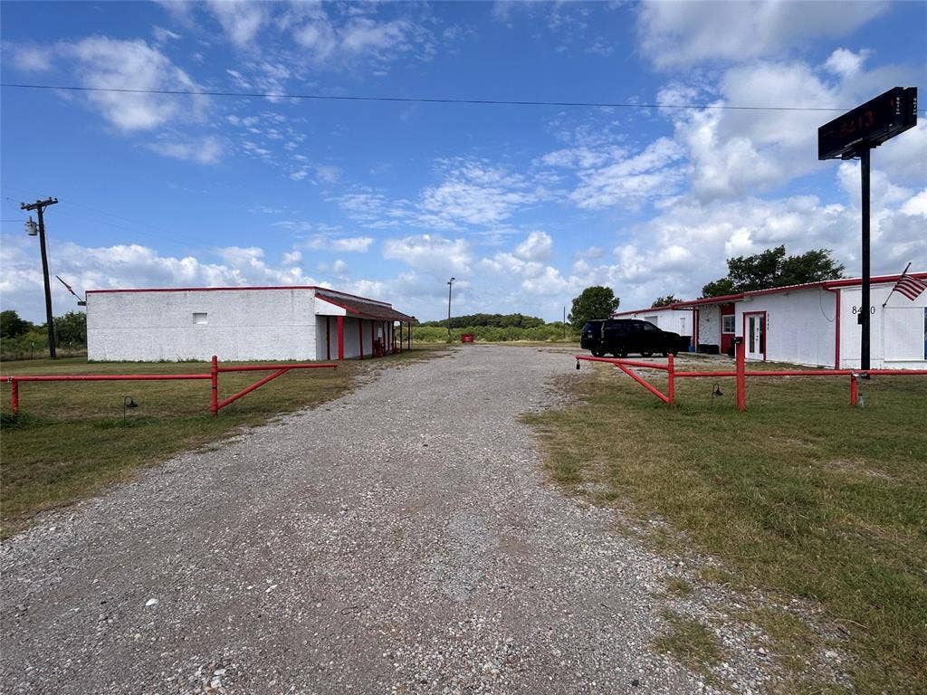 8440 E Highway 175 Highway, Kemp, TX 75143 Exterior of commercial structures featuring white masonry construction with red trim, a gravel surface, and red metal access gates