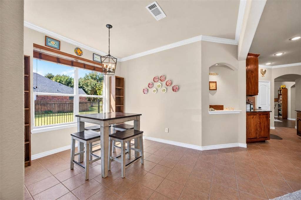 1514 Natalie Lane, Duncanville, TX 75137 Dining area featuring tile flooring, crown molding, an arched wall cutout, and a hanging metal pendant light fixture