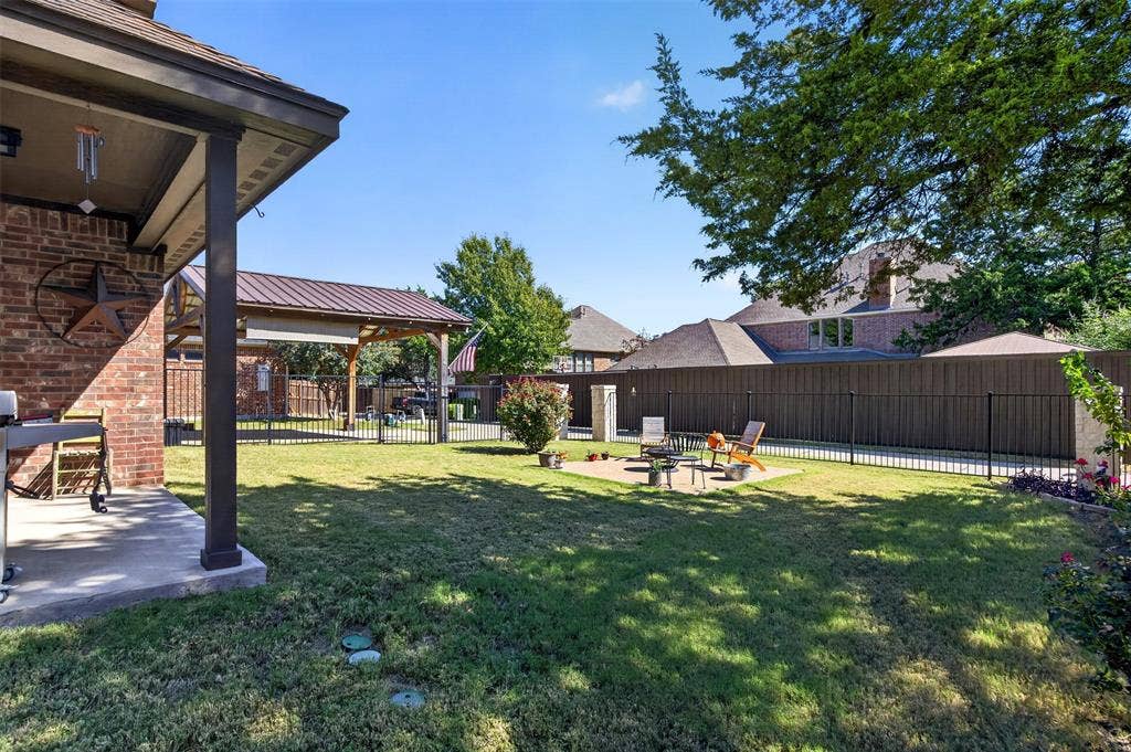 1514 Natalie Lane, Duncanville, TX 75137 Backyard featuring a covered brick patio, metal-roofed pavilion, stone-paver hardscaping, manicured lawn, and full-perimeter fencing
