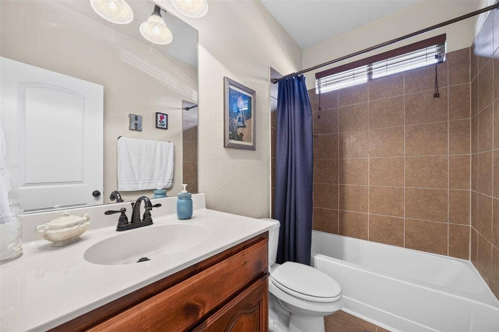 1514 Natalie Lane, Duncanville, TX 75137 Bathroom featuring a wood-finish vanity with a white countertop and oval undermount sink, three-light vanity fixture, and a tub-shower combination enclosed by brown tile surround