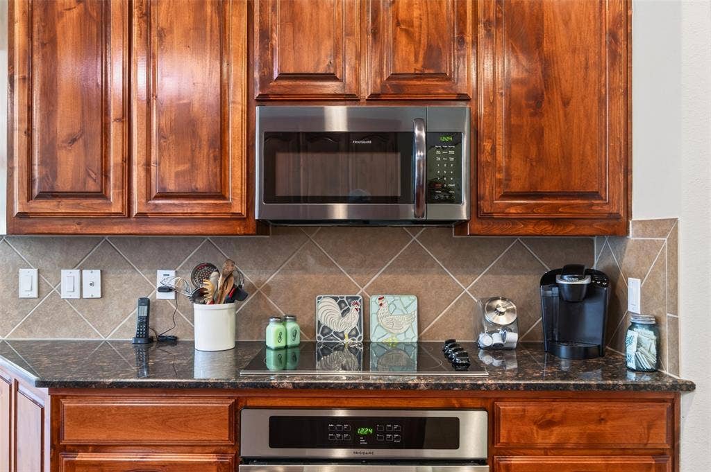 1514 Natalie Lane, Duncanville, TX 75137 Stained wood cabinetry, stainless steel microwave, dark stone-finish countertop, smooth-top electric cooktop, and diagonal-set tile backsplash