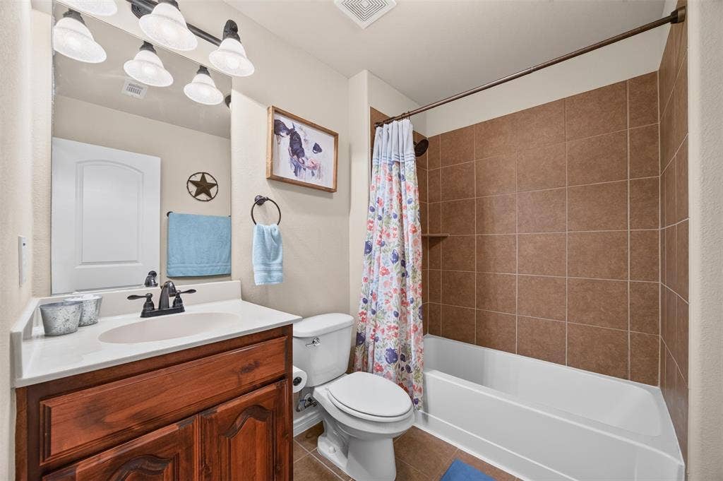 1514 Natalie Lane, Duncanville, TX 75137 Bathroom featuring a wood-finish vanity with an integrated basin, matte black faucet, wall-mounted light fixture, and a tub-shower combination with ceramic tile surround