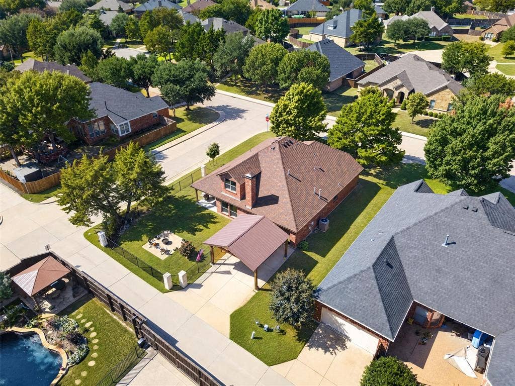 1514 Natalie Lane, Duncanville, TX 75137 Aerial perspective of a brick residence featuring a metal-roofed carport, a prominent chimney, a fenced perimeter, and established trees on a corner lot