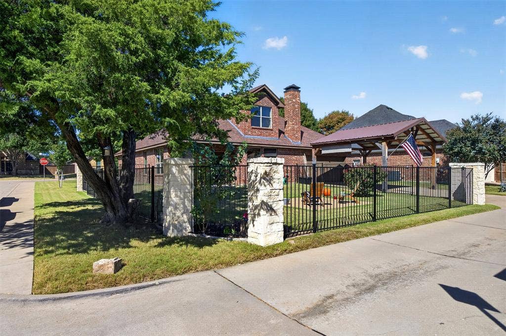 1514 Natalie Lane, Duncanville, TX 75137 Brick exterior featuring a multi-tiered roofline, stone-pillar metal fencing, and a detached covered pavilion