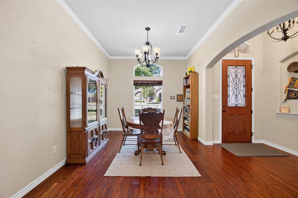 1514 Natalie Lane, Duncanville, TX 75137 Dining area featuring wood-finish flooring, crown molding, a central chandelier, and an arched window with transom detailing