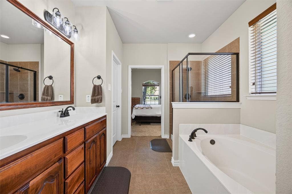 1514 Natalie Lane, Duncanville, TX 75137 Bathroom featuring a wood-tone vanity with a solid-surface countertop, soaking tub, glass-enclosed shower, and neutral tile flooring