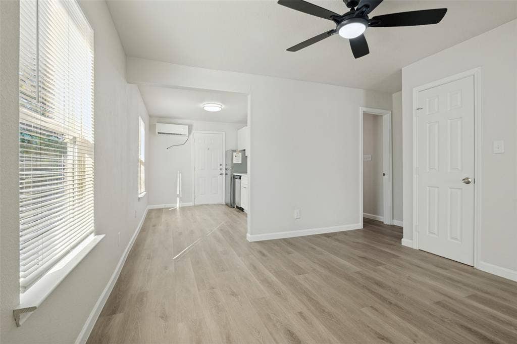 Wood-finish flooring, matte black ceiling fan with integrated lighting, wall-mounted ductless air conditioning unit, and white six-panel interior doors